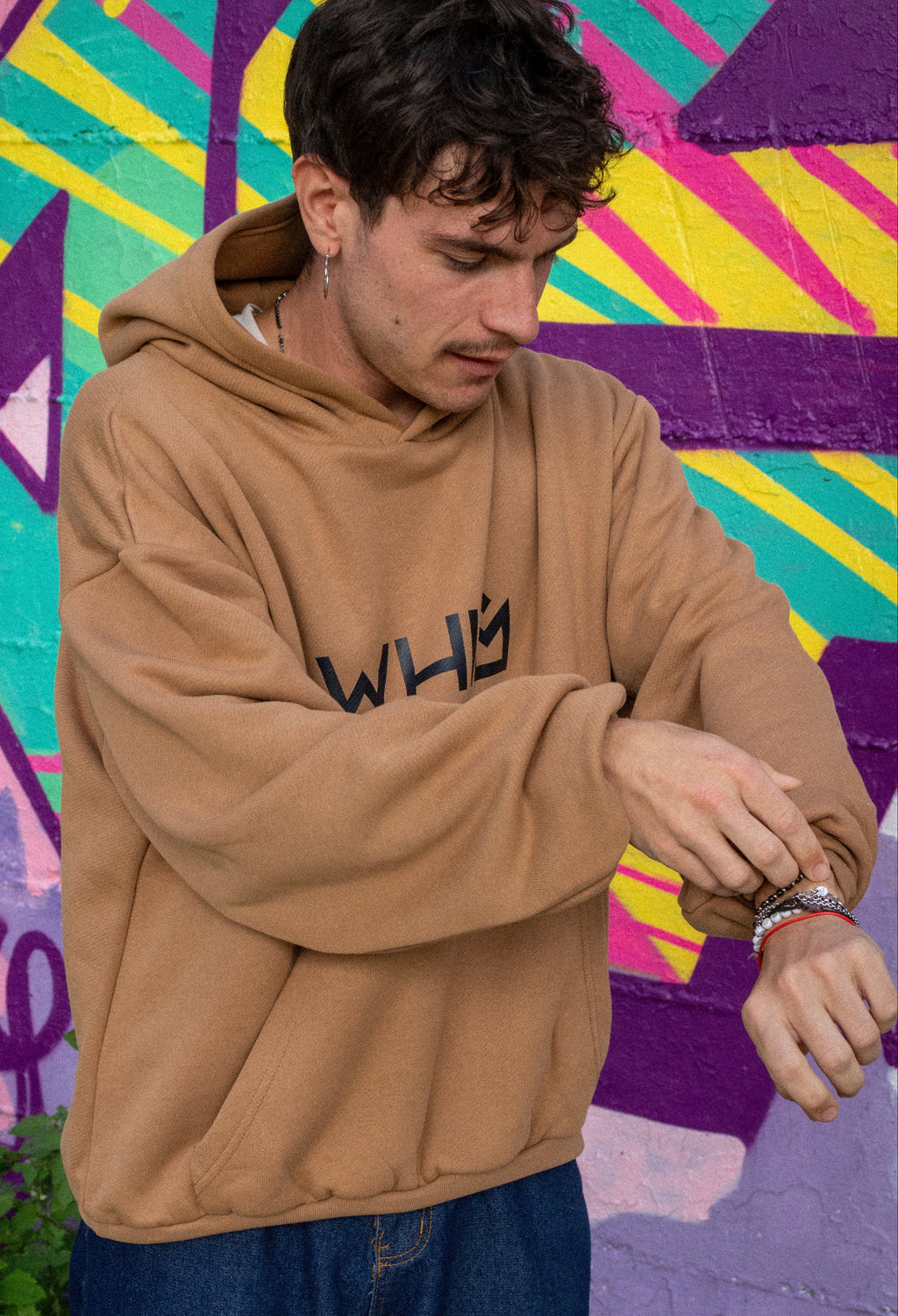 Un modello indossa una felpa unisex WHIM color cammello davanti a un muro con murales