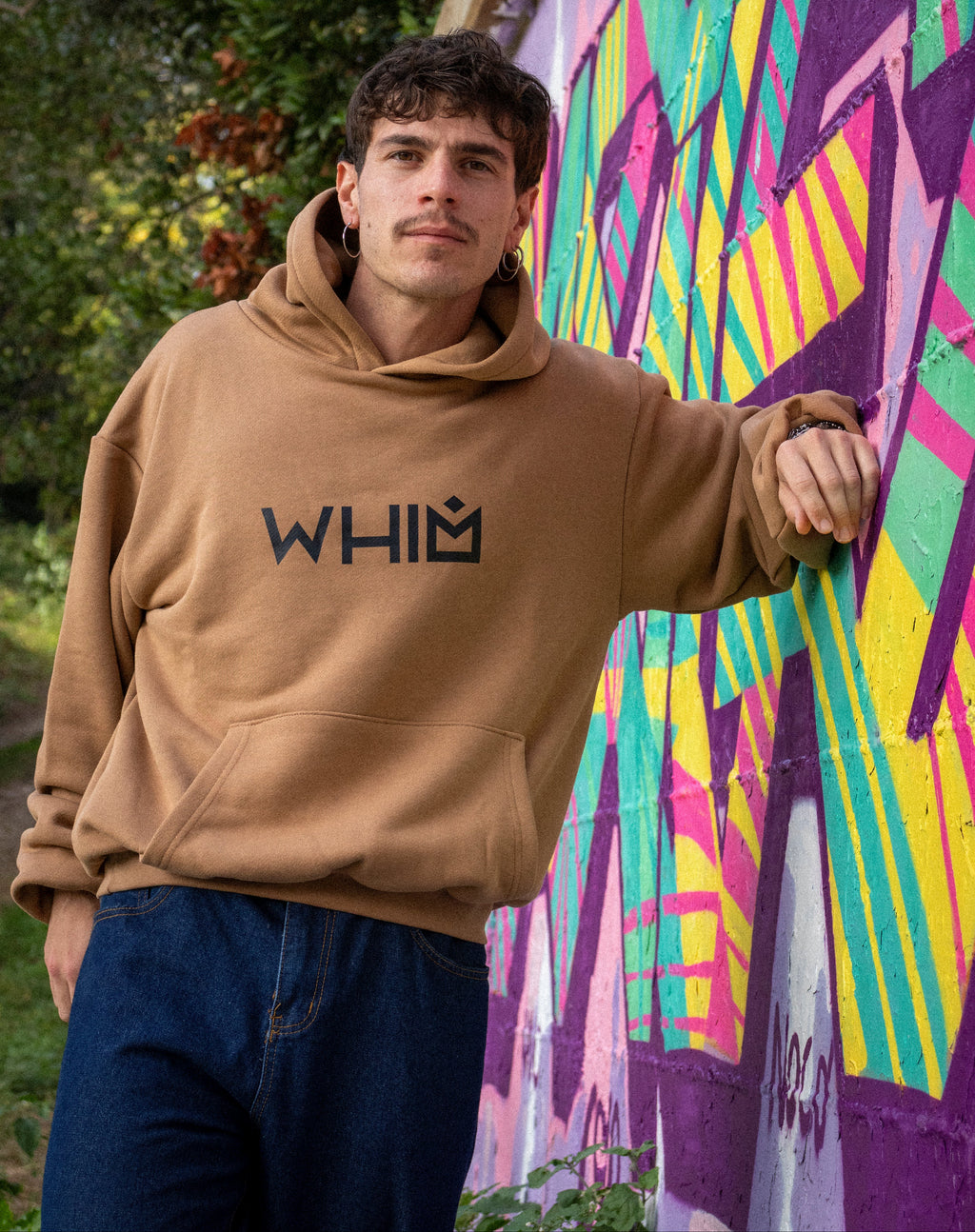 Modello che indossa una felpa WHIM color cammello in cotone premium, tessuto french terry pesante 480gsm, davanti a un muro con murales