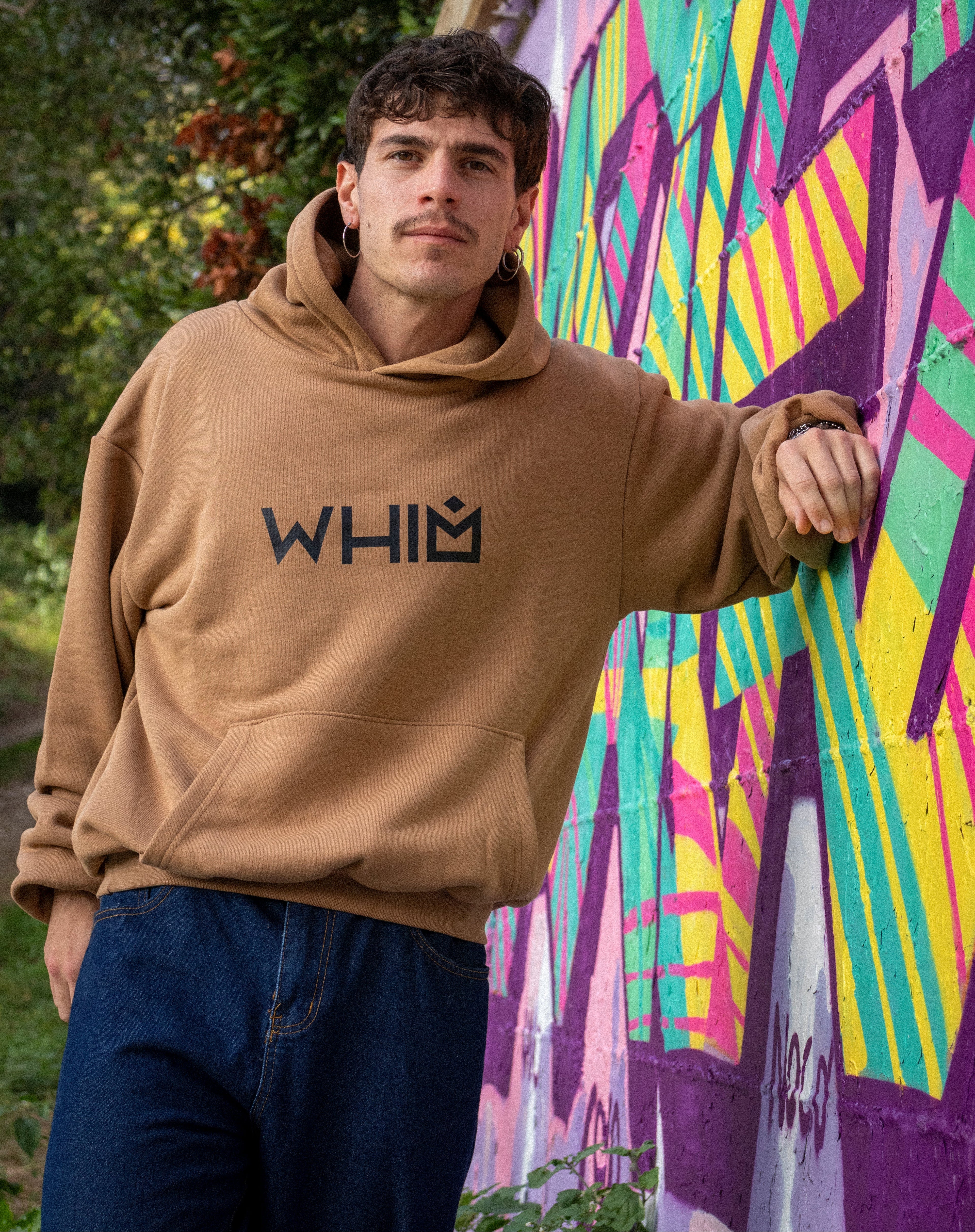 Modello che indossa una felpa WHIM color cammello in cotone premium, tessuto french terry pesante 480gsm, davanti a un muro con murales