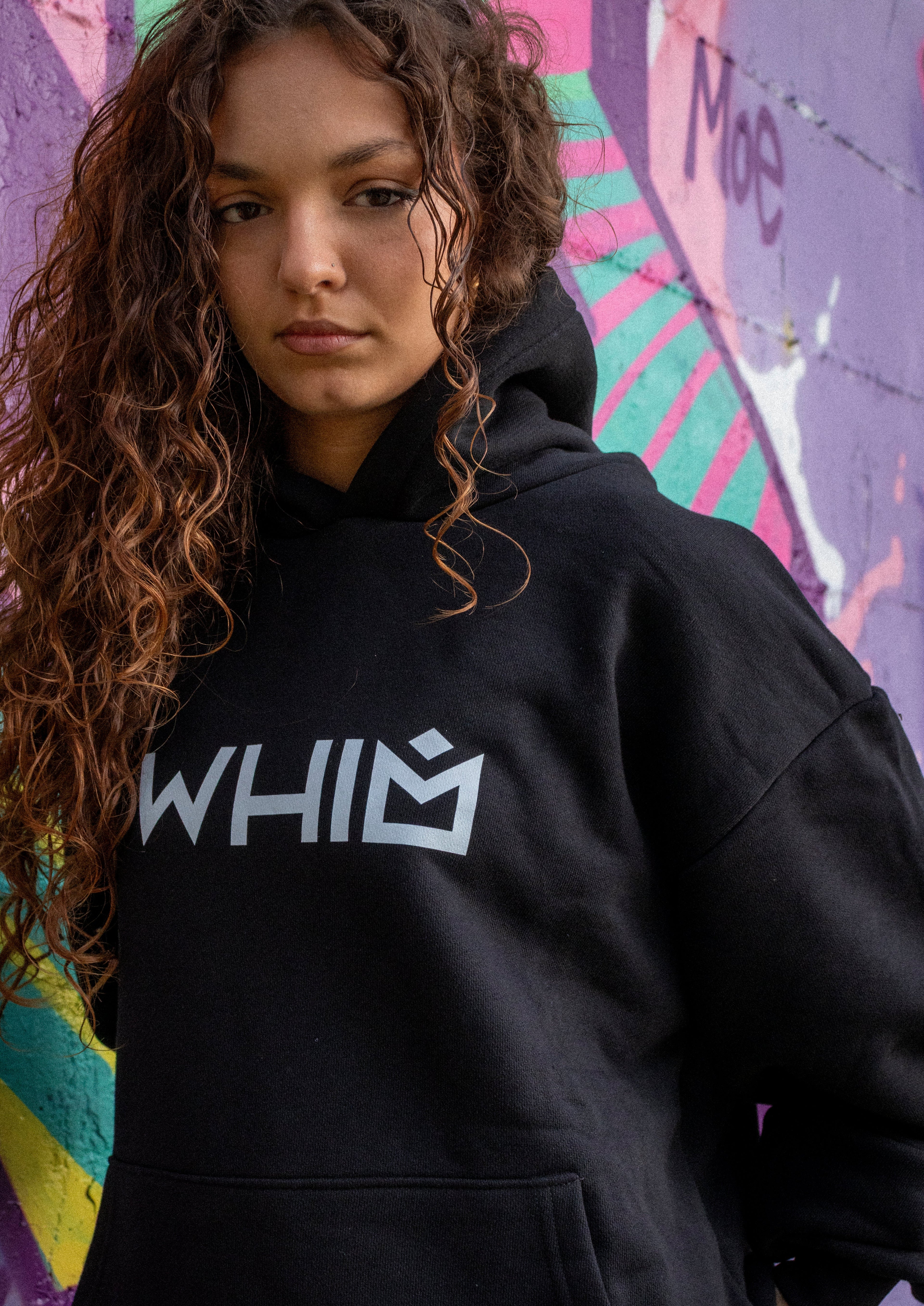 Felpa nera WHIM in cotone premium french terry pesante 480gsm indossata da una modella davanti a un muro con murales